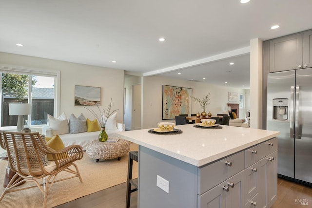 kitchen with gray cabinetry, a kitchen island, stainless steel refrigerator with ice dispenser, a kitchen breakfast bar, and dark wood-type flooring