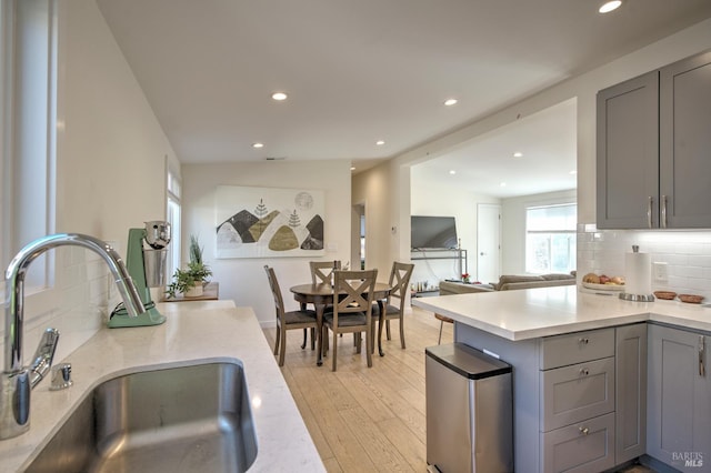 kitchen with light wood-type flooring, decorative backsplash, sink, and gray cabinetry