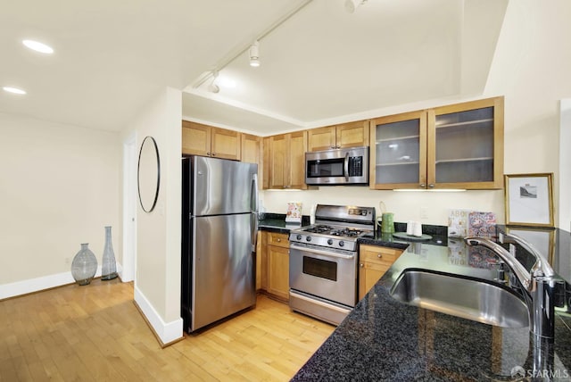 kitchen featuring rail lighting, sink, dark stone countertops, light wood-type flooring, and stainless steel appliances