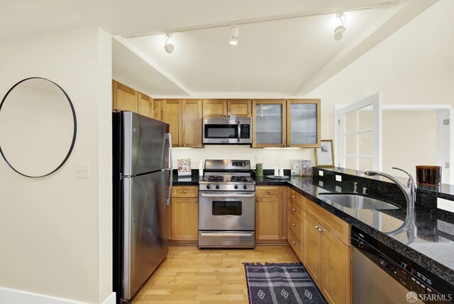 kitchen with rail lighting, stainless steel appliances, sink, dark stone countertops, and light hardwood / wood-style floors