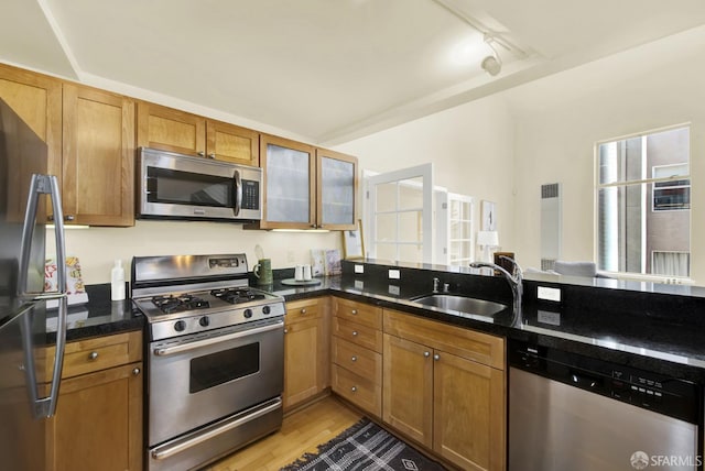 kitchen with rail lighting, sink, dark stone countertops, light hardwood / wood-style floors, and stainless steel appliances