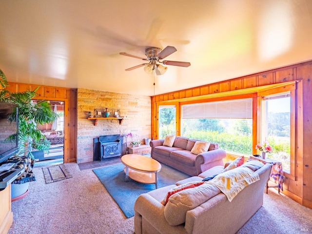 carpeted living room with a wood stove, wood walls, and ceiling fan