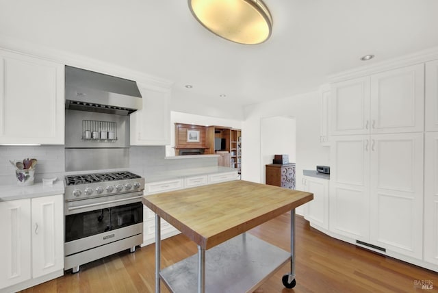 kitchen featuring wall chimney exhaust hood, tasteful backsplash, stainless steel range, white cabinetry, and light hardwood / wood-style flooring