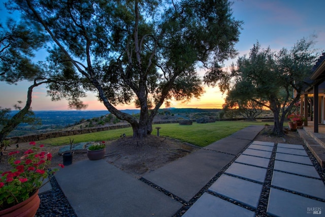 patio terrace at dusk featuring a lawn