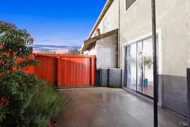 property exterior at dusk featuring a patio, fence, and stucco siding