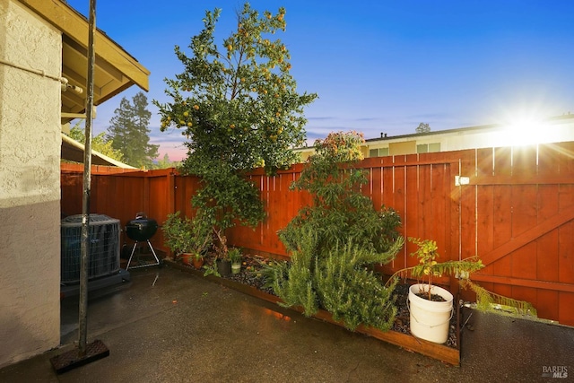 patio terrace at dusk featuring a fenced backyard and central AC unit