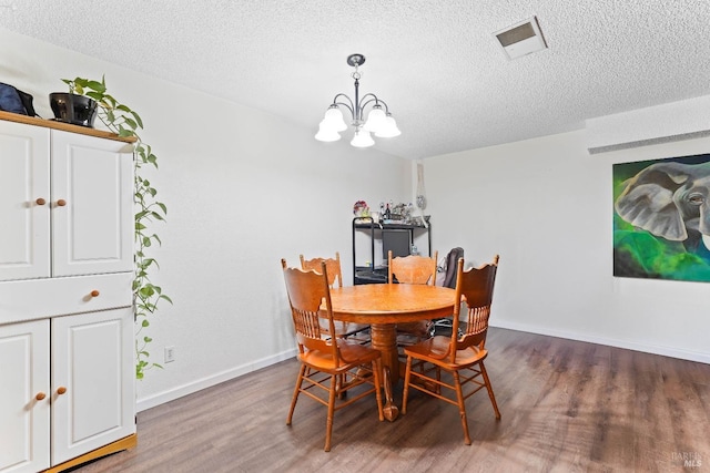 dining room featuring visible vents, a textured ceiling, an inviting chandelier, and wood finished floors