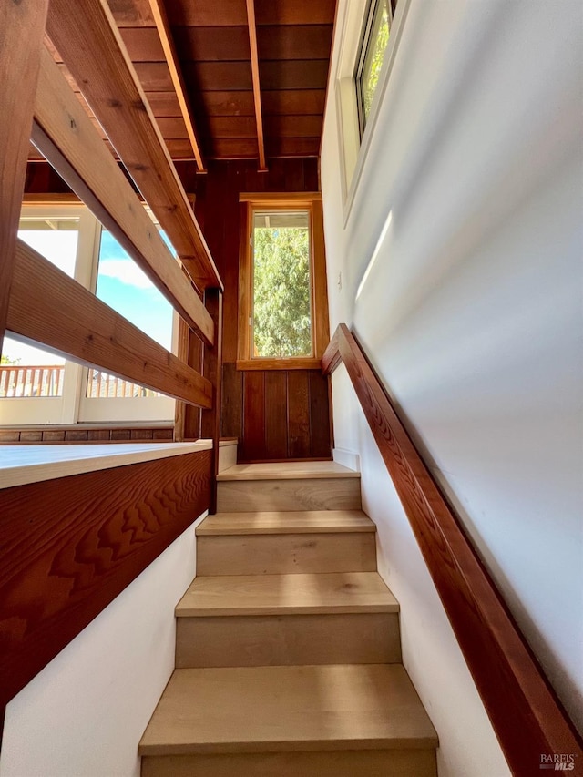 staircase featuring wood walls, wooden ceiling, and beamed ceiling