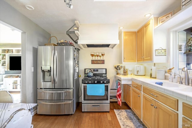 kitchen with sink, ventilation hood, tile countertops, appliances with stainless steel finishes, and light wood-type flooring