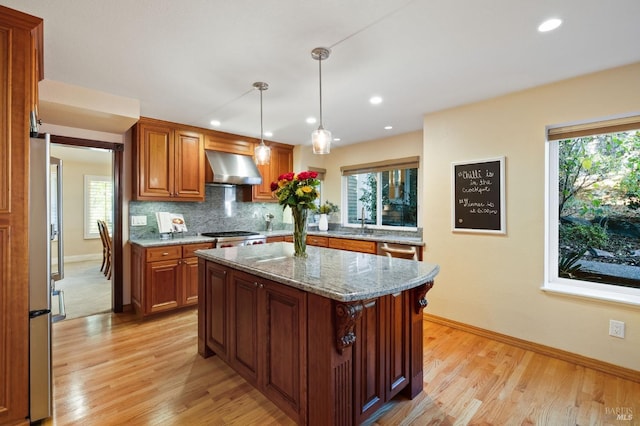 kitchen with a center island, hanging light fixtures, sink, light stone counters, and extractor fan