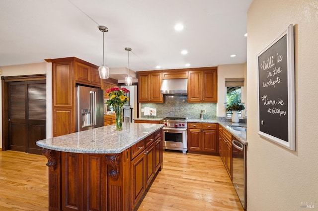 kitchen with high quality appliances, light hardwood / wood-style flooring, pendant lighting, and range hood