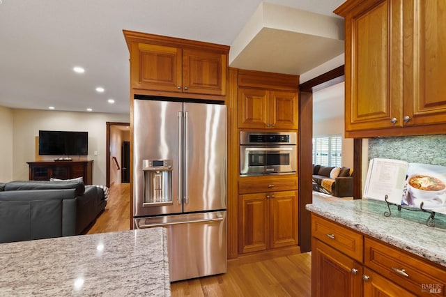 kitchen featuring decorative backsplash, light stone counters, stainless steel appliances, and light wood-type flooring