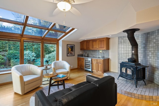 living room with wine cooler, light hardwood / wood-style floors, a wood stove, and ceiling fan