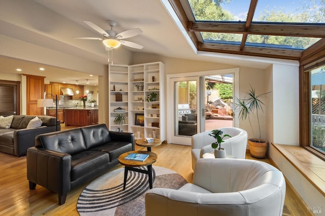 living room featuring light wood-type flooring, ceiling fan, and vaulted ceiling with skylight