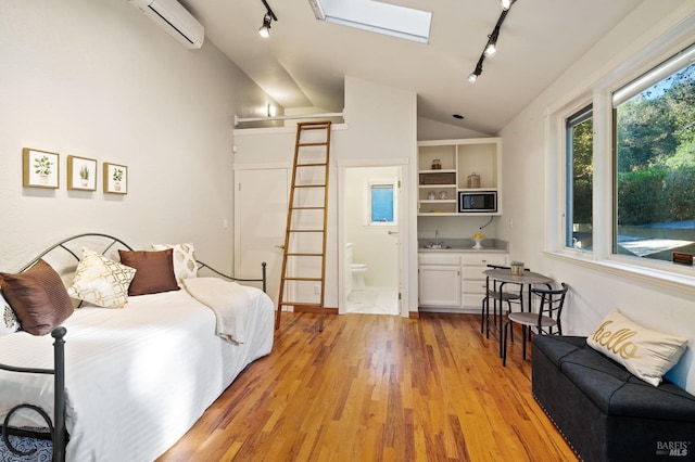 bedroom featuring a wall mounted air conditioner, light wood-type flooring, track lighting, lofted ceiling with skylight, and sink