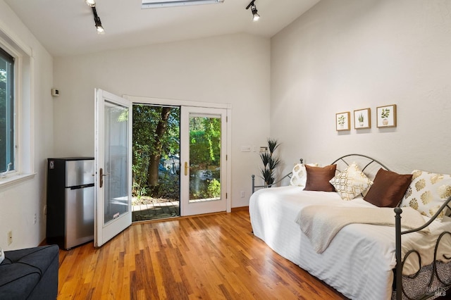 bedroom featuring access to exterior, lofted ceiling, light hardwood / wood-style flooring, and track lighting