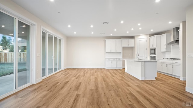 kitchen with a center island with sink, white cabinets, light wood-type flooring, and wall chimney exhaust hood