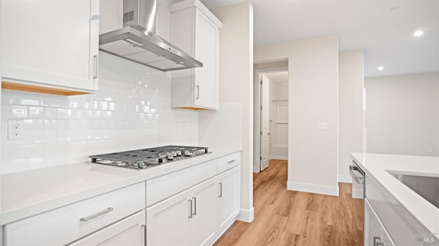 kitchen featuring wall chimney range hood, decorative backsplash, stainless steel gas stovetop, and white cabinets