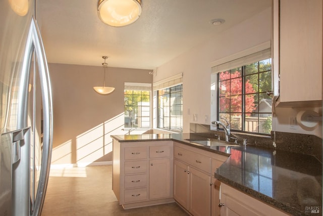 kitchen featuring decorative light fixtures, stainless steel refrigerator, sink, dark stone countertops, and kitchen peninsula