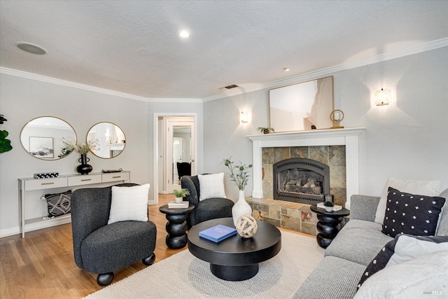 living area featuring a tile fireplace, wood finished floors, a textured ceiling, visible vents, and ornamental molding