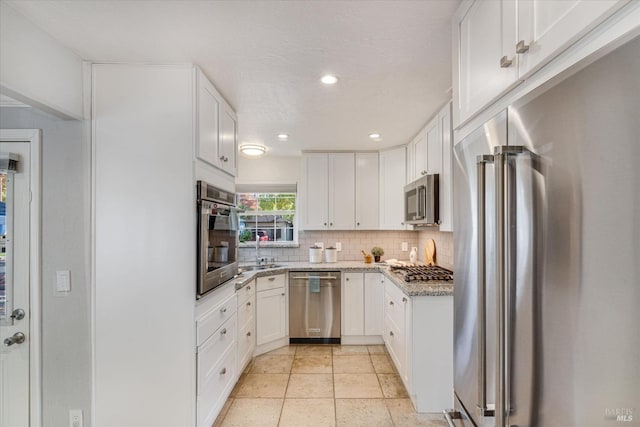 kitchen with stainless steel appliances, decorative backsplash, a sink, light stone counters, and white cabinets