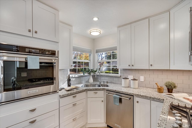 kitchen with light stone counters, backsplash, a sink, stainless steel appliances, and white cabinets