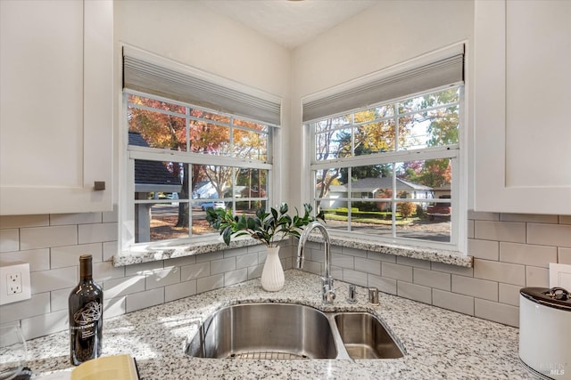 kitchen with white cabinetry, backsplash, a sink, and light stone counters