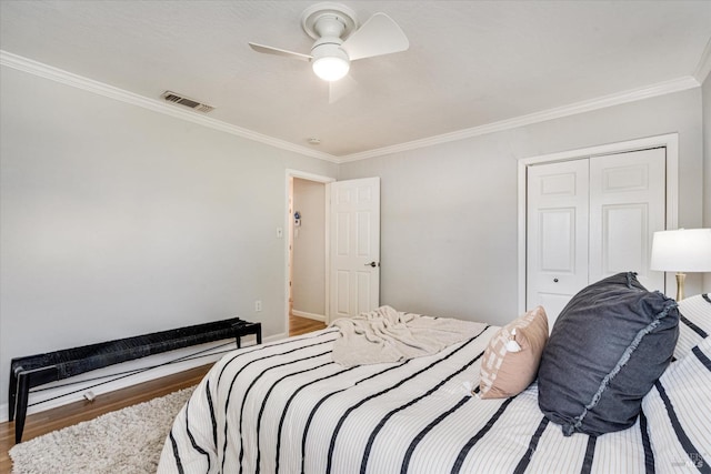bedroom with a closet, visible vents, ornamental molding, wood finished floors, and a ceiling fan