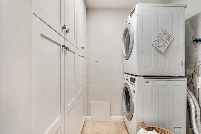 laundry room with a textured wall, cabinet space, stacked washer / dryer, and baseboards