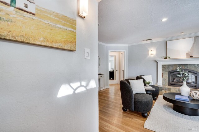 living room with crown molding, a tile fireplace, a textured ceiling, light wood-type flooring, and visible vents
