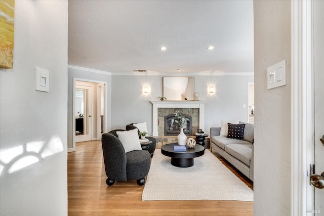 living room with visible vents, light wood-style flooring, crown molding, and a tile fireplace