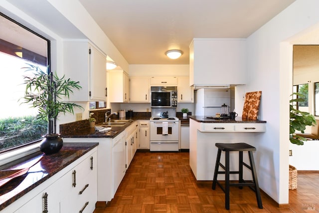 kitchen featuring a breakfast bar, electric range, white cabinets, a sink, and dark stone counters