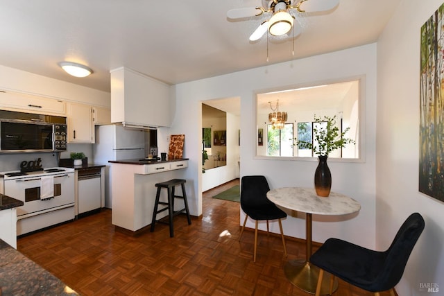 kitchen featuring dark countertops, white appliances, white cabinets, and ceiling fan with notable chandelier