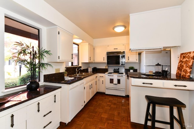 kitchen with dark stone counters, white appliances, a sink, and white cabinetry