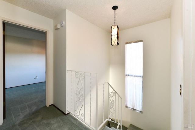 hallway with a textured ceiling, dark carpet, and an upstairs landing