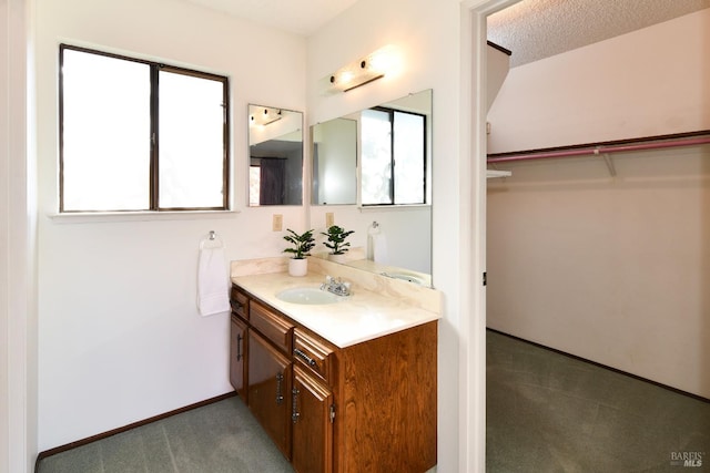 bathroom with a walk in closet, vanity, baseboards, and a textured ceiling