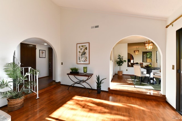 entryway featuring arched walkways, visible vents, a towering ceiling, wood finished floors, and a chandelier