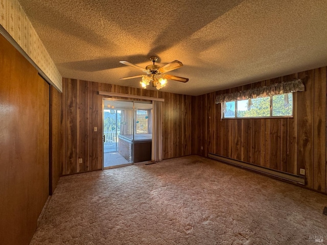 unfurnished room featuring wooden walls, a baseboard radiator, carpet, ceiling fan, and a textured ceiling