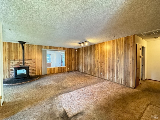 unfurnished living room featuring carpet flooring, a wood stove, a textured ceiling, and wooden walls