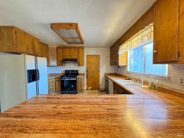 kitchen featuring sink, white refrigerator with ice dispenser, stainless steel dishwasher, kitchen peninsula, and black range