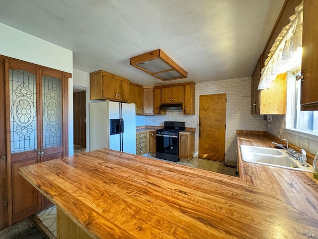 kitchen with black gas range oven, sink, white refrigerator with ice dispenser, and kitchen peninsula