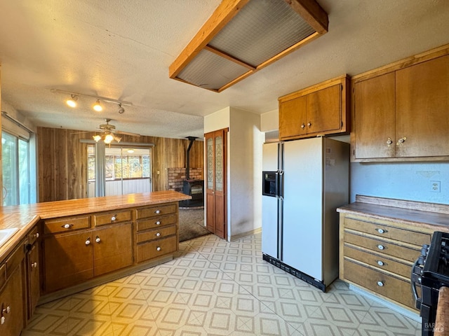 kitchen featuring wooden walls, a wood stove, white fridge with ice dispenser, black gas stove, and a textured ceiling