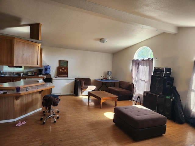 living room with light wood-type flooring, a textured ceiling, and vaulted ceiling with beams