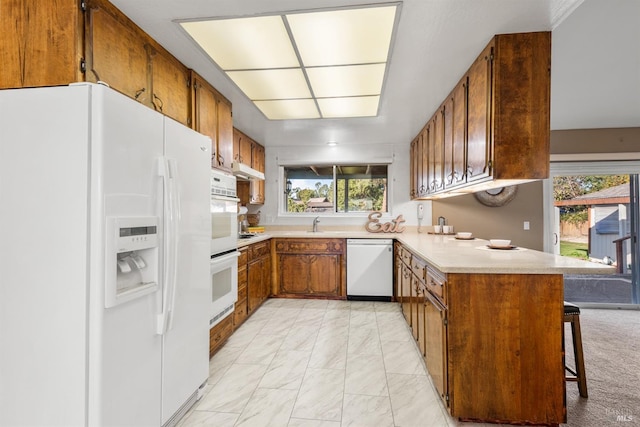 kitchen with a kitchen bar, sink, white appliances, and kitchen peninsula