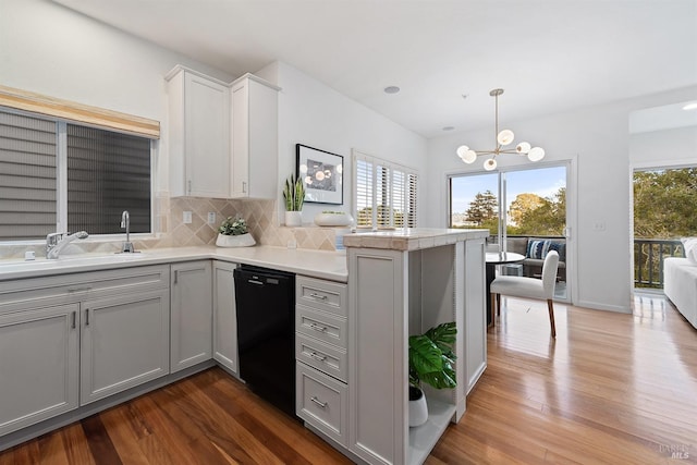 kitchen with dark wood-type flooring, dishwasher, hanging light fixtures, backsplash, and kitchen peninsula