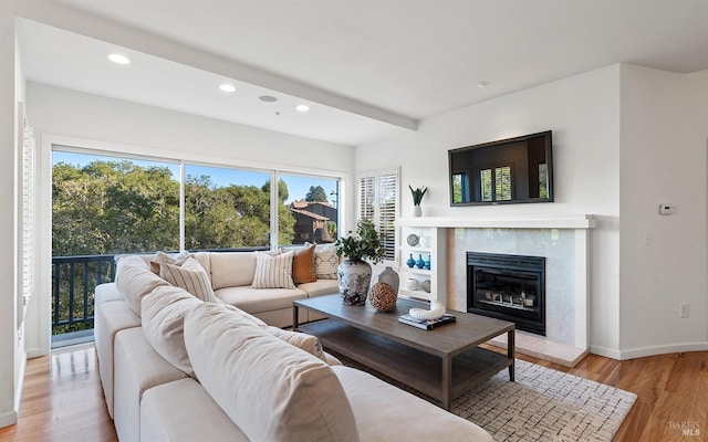 living room featuring beamed ceiling, a healthy amount of sunlight, a fireplace, and light hardwood / wood-style floors