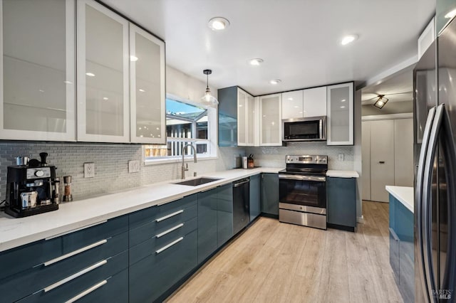 kitchen with white cabinetry, sink, stainless steel appliances, pendant lighting, and light hardwood / wood-style floors