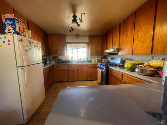 kitchen featuring gas range, sink, white refrigerator, a textured ceiling, and light tile patterned floors