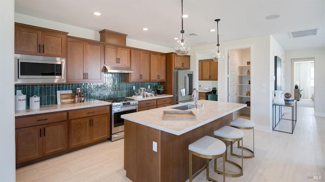 kitchen with sink, pendant lighting, a kitchen island with sink, a breakfast bar, and appliances with stainless steel finishes