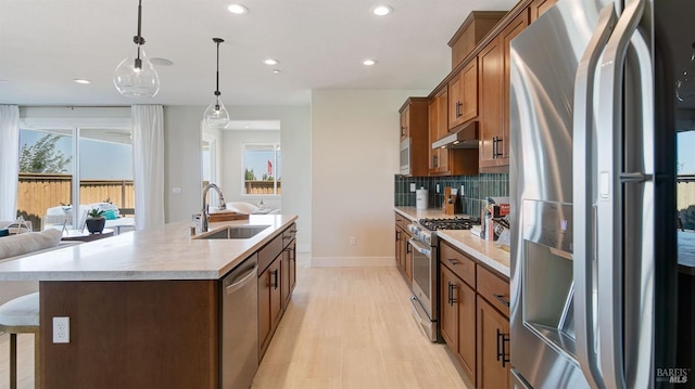 kitchen with sink, stainless steel appliances, tasteful backsplash, an island with sink, and decorative light fixtures